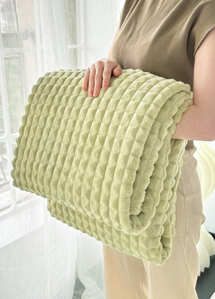 Person holding a light green textured blanket indoors
