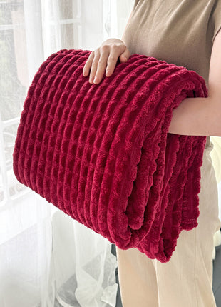 Person holding a red textured blanket in front of a window with white curtains.