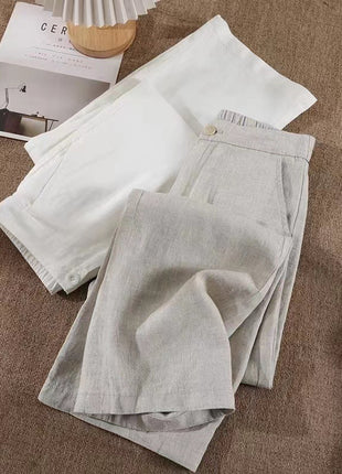 Light gray linen pants on a brown fabric surface with a magazine and small wooden item.