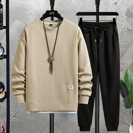 Beige sweatshirt and black pants on hangers against a textured wall.