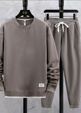 Brown sweatshirt and pants set on hangers against a gray textured wall.