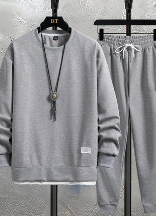 Gray sweatshirt and pants set on hangers against a textured wall.