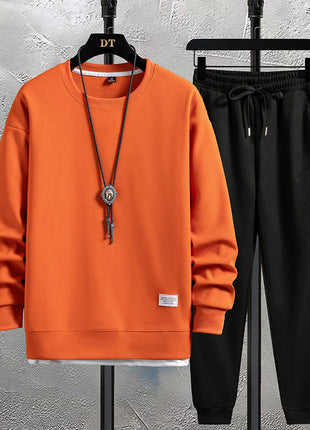 Orange sweatshirt and black pants on hangers against a textured wall.