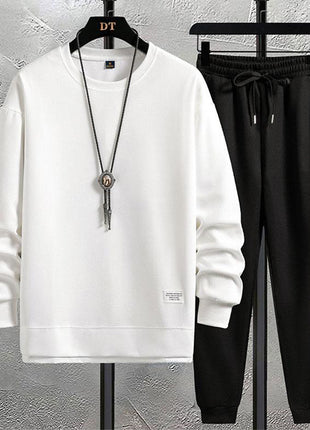 White sweatshirt and black pants on hangers against a gray wall.