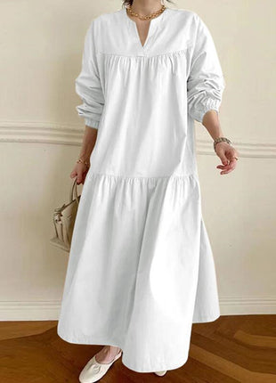 Person wearing a white dress with long sleeves in a room with wooden flooring and a neutral wall.