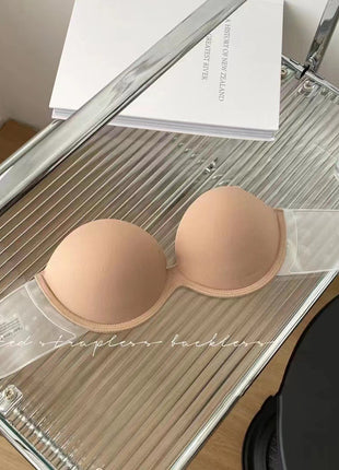 Nude-colored strapless bra on a clear plastic stand with a mirror in the background.