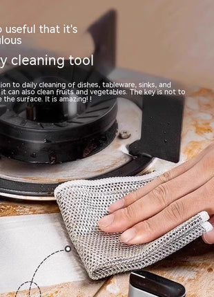 Person cleaning a stove with a mesh cleaning tool on a kitchen counter.