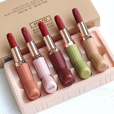 A set of five HOJO lipsticks in various colors displayed in a box with a velvet texture finish.