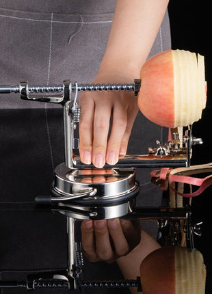 Person using an apple peeler with a sliced apple on a reflective surface.