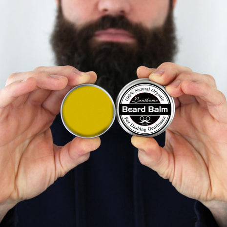 Two containers of beard balm held by hands with a blurred background