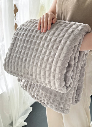 Person holding a textured gray blanket in front of a window with sheer curtains.