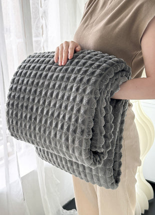 Person holding a textured gray blanket in a bright room with white curtains.