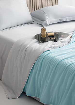 Bed with white bedding and a light blue throw blanket, featuring a small tray with items on a nightstand.