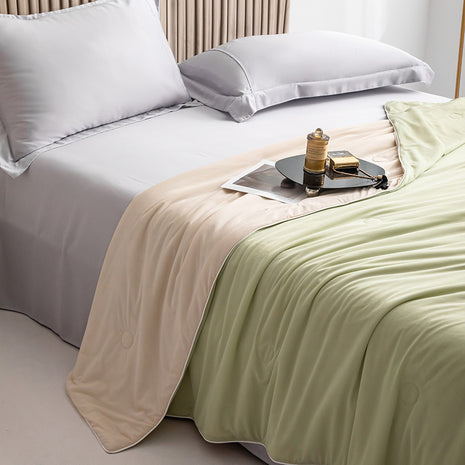 Bed with white bedding and a tray with a cup and book on a beige and green blanket.