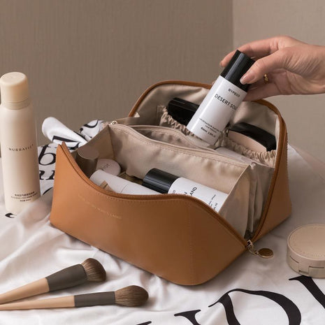 Brown cosmetic bag with skincare products and makeup brushes on a light background