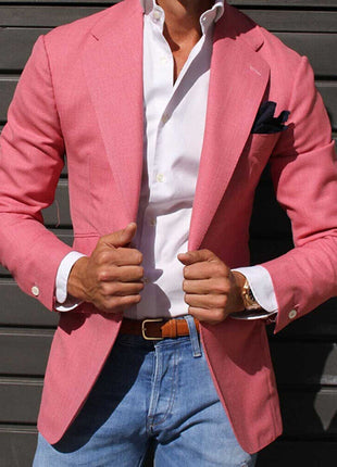 Person wearing a pink blazer over a white shirt with blue jeans against a dark background