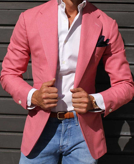 Person wearing a pink blazer over a white shirt with blue jeans against a dark background