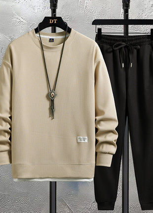 Beige sweatshirt and black pants on hangers against a textured wall.