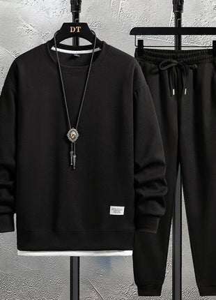 Black hoodie and pants set on hangers against a textured wall.
