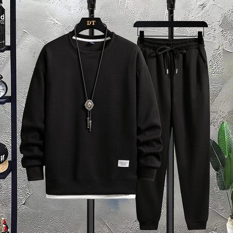 Black hoodie and pants set on hangers against a textured wall.