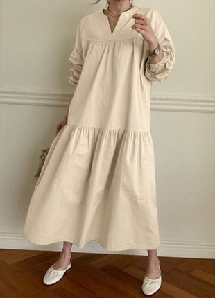 Person wearing a beige dress in an indoor setting with wooden flooring and white walls.