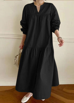 Person wearing a black long-sleeve dress against a white wall.