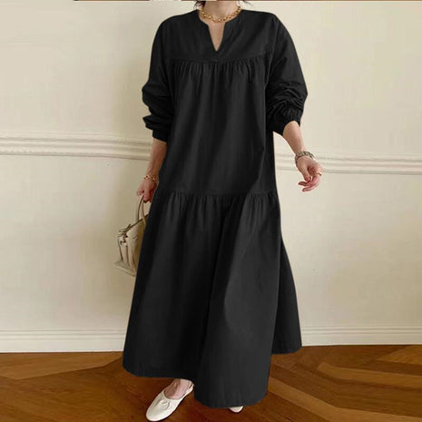 Person wearing a black long-sleeve dress against a white wall.