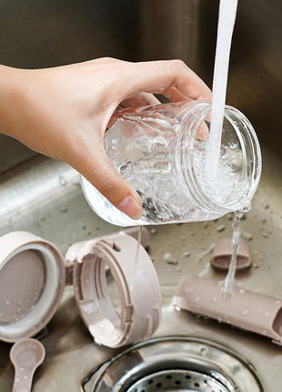 Person washing a glass jar over a sink with cleaning supplies nearby