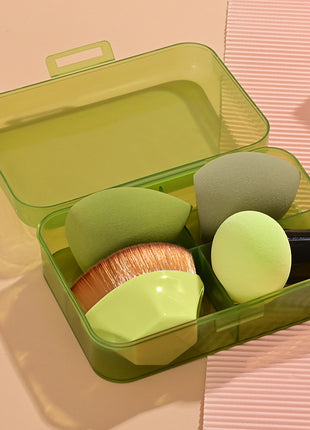 Set of makeup sponges and brushes in a green case on a pink surface