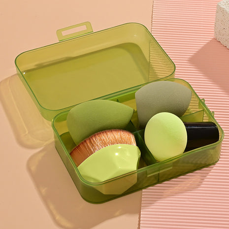 Set of makeup sponges and brushes in a green case on a pink surface