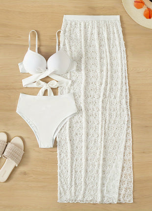 White bikini set and lace skirt on a wooden surface with sandals.