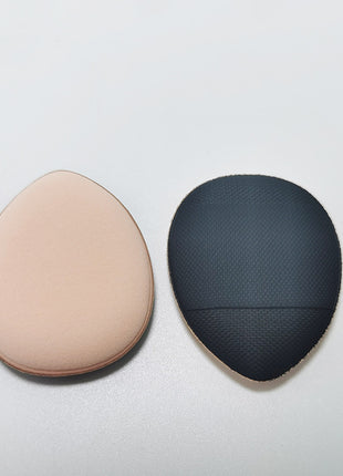 Two makeup sponges, one beige and one black textured, on a light gray background.