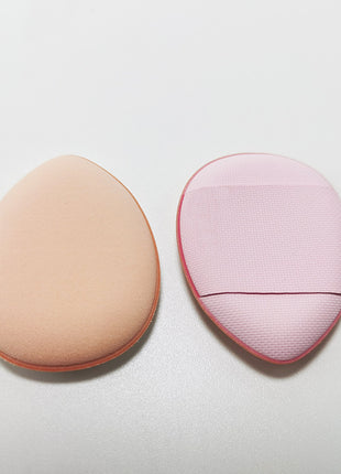 Two makeup sponges, one beige and one pink with a textured edge, on a light gray background.