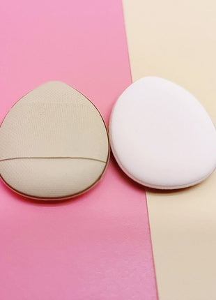 Two makeup sponges, one beige and one white, on a pink and beige gradient background.