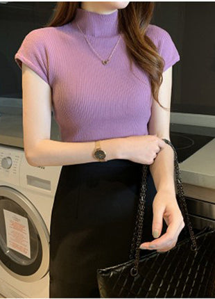 Person wearing a purple ribbed top and black pants in a kitchen.