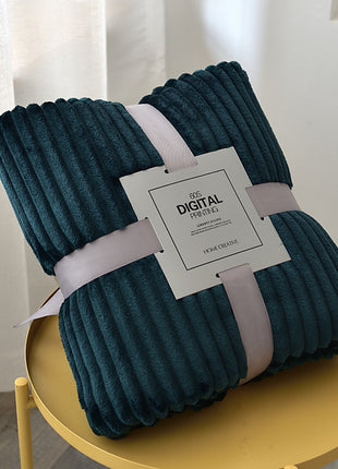 Folded teal blanket with a label on a yellow stool against a light curtain background